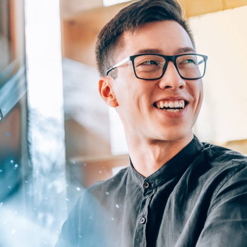 Asian man with glasses smiling off to the side, looking off into the distance